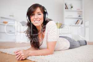 Charming brunette female using headphones while lying on a carpe