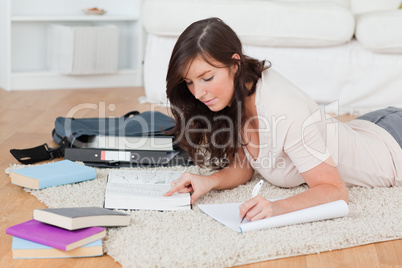 Young brunette female writing on a notebook while lying on a car