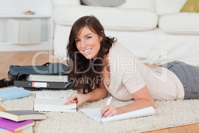 Young good looking female writing on a notebook while lying on a