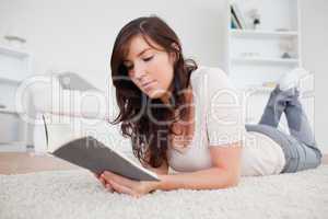 Young gorgeous woman reading a book while lying on a carpet