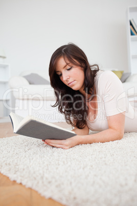 Young beautiful woman reading a book while lying on a carpet