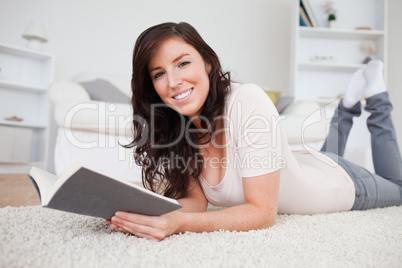 Young good looking woman reading a book while lying on a carpet