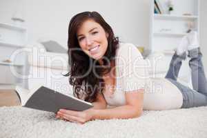 Young good looking woman reading a book while lying on a carpet