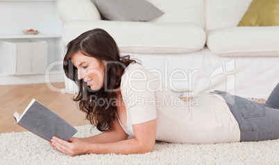Young pretty woman reading a book while lying on a carpet