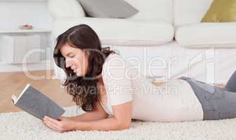 Young pretty woman reading a book while lying on a carpet