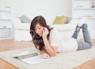Young beautiful female reading a magazine while lying on a carpe