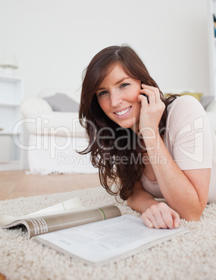 Young charming female reading a magazine while lying on a carpet