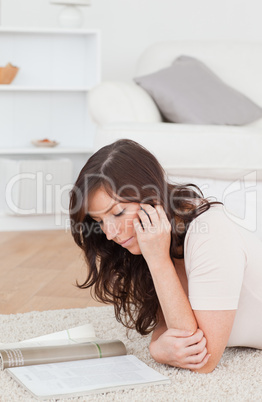 Young gorgeous female reading a magazine while lying on a carpet