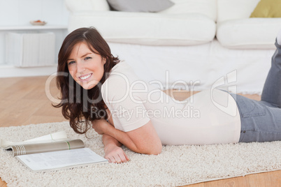 Young attractive woman reading a magazine while lying on a carpe