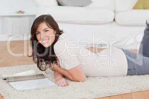 Young attractive woman reading a magazine while lying on a carpe