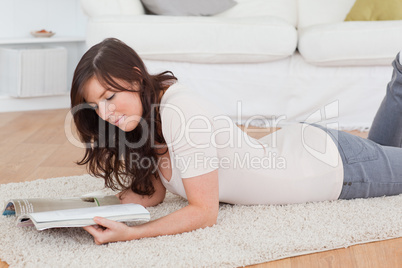 Young charming woman reading a magazine while lying on a carpet