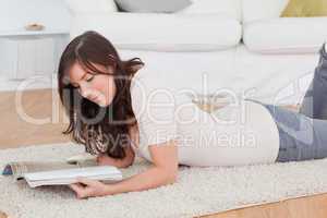 Young charming woman reading a magazine while lying on a carpet