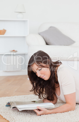 Young pretty woman reading a magazine while lying on a carpet