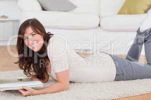 Young cute woman reading a magazine while lying on a carpet