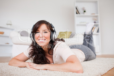 Good looking brunette female using headphones while lying on a c