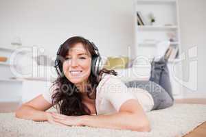 Good looking brunette female using headphones while lying on a c