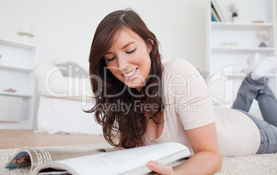 Gorgeous woman reading a magazine while lying on a carpet