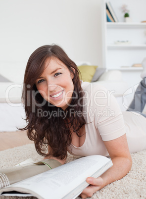 Beautiful woman reading a magazine while lying on a carpet