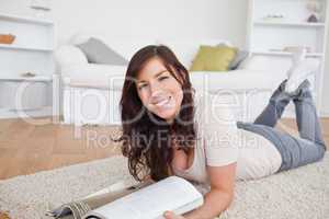 Good looking woman reading a magazine while lying on a carpet