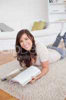 Charming woman reading a magazine while lying on a carpet
