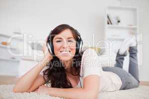 Gorgeous brunette female using headphones while lying on a carpe