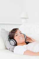 Charming brunette female relaxing with her headphones while lyin