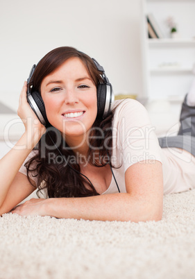 Charming brunette woman using headphones while lying on a carpet