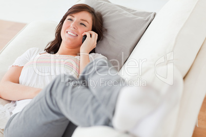 Pretty brunette female on the phone while lying on a sofa