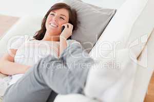 Pretty brunette female on the phone while lying on a sofa