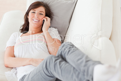 Cute brunette female on the phone while lying on a sofa