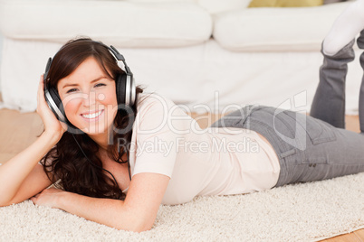 Beautiful brunette woman using headphones while lying on a carpe