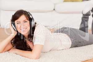 Beautiful brunette woman using headphones while lying on a carpe
