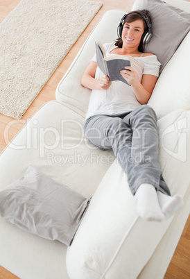 Young attractive female reading a book while lying on a sofa