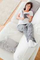 Young pretty female reading a book while lying on a sofa