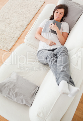 Young cute female having a rest and reading a book while lying o