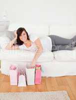 Young cute female posing with her shopping bags while lying on a