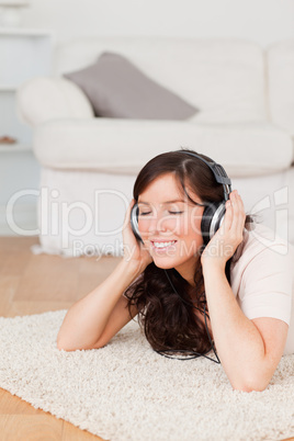 Good looking brunette woman using headphones while lying on a ca