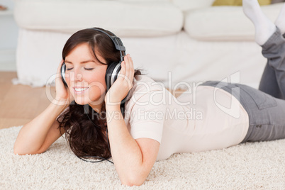 Cute brunette woman using headphones while lying on a carpet