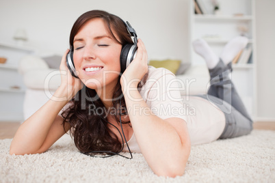 Smiling brunette woman using headphones while lying on a carpet