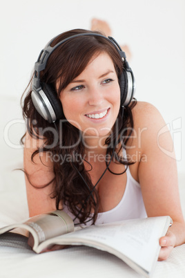 Cute female with headphones reading a magazine while lying