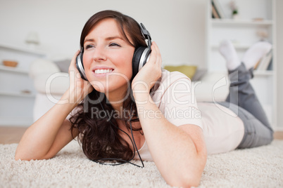 Cheerful brunette woman using headphones while lying on a carpet