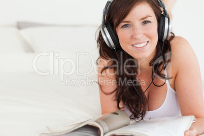 Good looking female with headphones reading a magazine while lyi