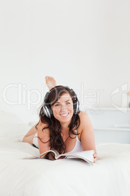 Charming female with headphones reading a magazine while lying