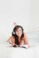 Charming female with headphones reading a magazine while lying