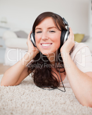 Cute smiling woman using headphones while lying on a carpet