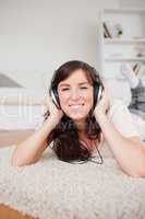 Pretty smiling woman using headphones while lying on a carpet