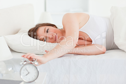 Lovely brunette woman turning off a clock while lying