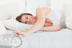 Lovely brunette woman turning off a clock while lying