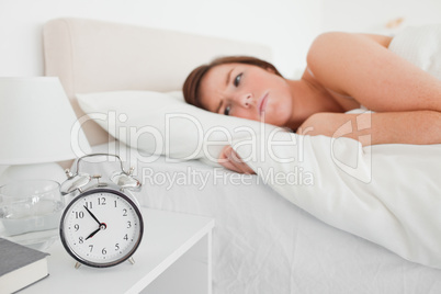 Lovely brunette woman awaking with a clock while lying