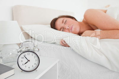 Charming brunette woman awaking with a clock while lying